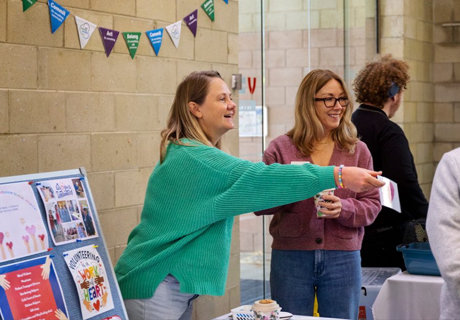 Two women standing, one is offering a flyer out. There are people in the background.