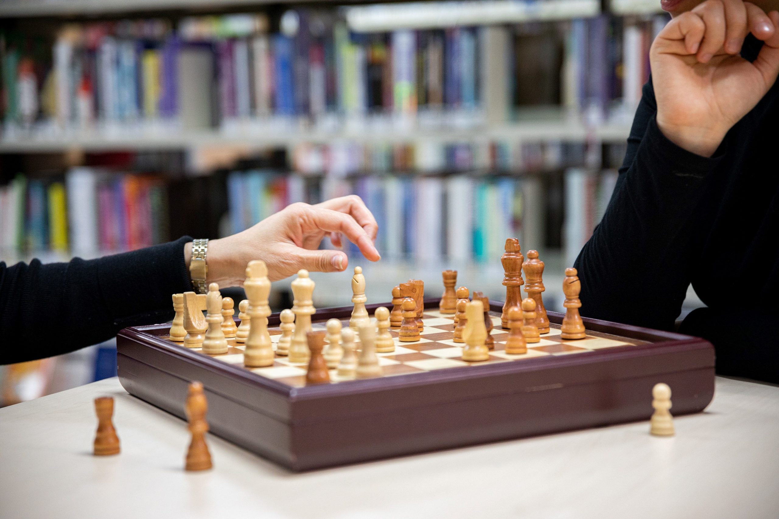 Two people playing chess in a library.