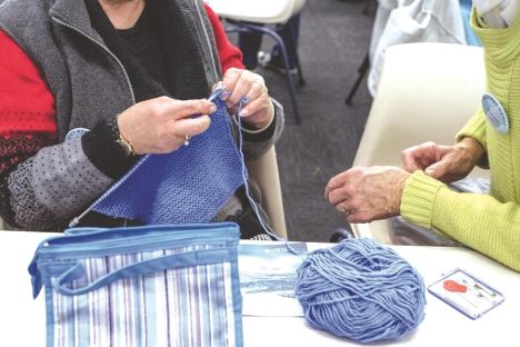 Two people siting together while one is knitting. 